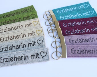 May include: Keychains in various colors, each featuring the embroidered text "Erzieherin mit" and a heart symbol. The keychains are made of felt and have a metal clasp for attaching keys.