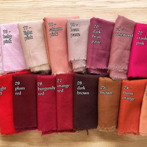 May include: A collection of rectangular fabric swatches arranged in two rows, each labelled with a number and colour name including baby pink, salmon pink, rosewood, cranberry pink, bright red, plum red, burgundy, and various shades of brown.