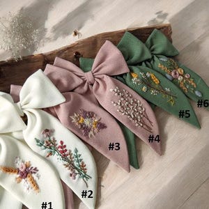 Puede incluir: Seis lazos para el pelo hechos a mano de tela con dise&ntilde;os florales bordados en tonos verdes, rosas y blancos. Los lazos est&aacute;n numerados del 1 al 6.