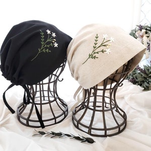 Peut inclure: Deux chapeaux en tissu avec des motifs floraux brodés. Le chapeau de gauche est noir et le chapeau de droite est beige.