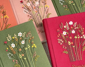 Könnte beinhalten: Vier bestickte Notizbücher mit Blumendesigns. Die Notizbücher sind in den Farben Rosa, Grün und Rot gehalten. Die Namen "Cherry", "Helen" und "Denise" sind auf den Einbänden gestickt.