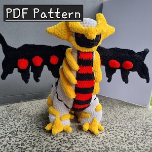 May include: A crocheted plush toy of a mythical creature, featuring yellow, black, red, and white yarn. The wings are black with red accents. The text "PDF Pattern" is displayed at the top of the image.