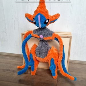 Könnte beinhalten: Handgefertigtes Plüschtier eines Deoxys-Pokémon-Charakters mit orange, blauen und grauen Farben. Das Plüschtier hat eine markante Kopfform und lange, flexible Gliedmaßen. Der Text "PDF Pattern" ist sichtbar.