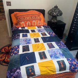 May include: A bed with a patchwork quilt featuring tarot card images, blue, yellow, and white squares. An orange pillow with a patterned design rests on the bed. A decorative rug with a butterfly design is on the floor.