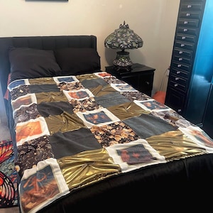 May include: A patchwork quilt with a black velvet base, featuring squares of gold, black, and patterned fabrics. Some squares display images. The quilt is on a black bed, with black pillows and a black headboard. A framed picture hangs on the wall.