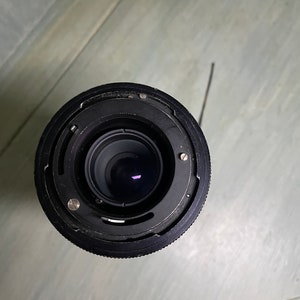 Puede incluir: Un objetivo de c&aacute;mara negro con un anillo plateado alrededor del borde. El objetivo est&aacute; sobre una superficie azul claro.