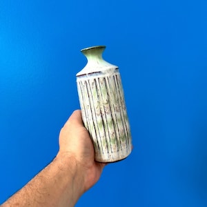 May include: A white ceramic vase with green and brown stripes. The vase has a textured surface and a rounded shape.