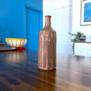 May include: A brown and yellow ceramic vase with a textured surface. The vase has a narrow neck and a wide base.