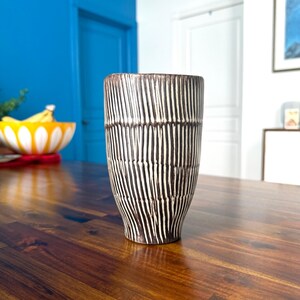 May include: A brown ceramic vase with a white striped pattern. The vase is sitting on a wooden table.