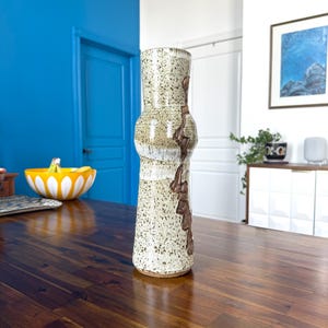 May include: A white ceramic vase with brown and gray speckles and a brown glaze. The vase has a rounded body and a narrow neck.