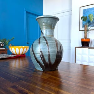 May include: A large, green and brown ceramic vase with a wide mouth and a narrow neck. The vase has a mottled glaze and a striped pattern.