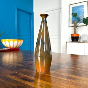 May include: A tall, brown and green ceramic vase with a rounded bottom and a narrow neck. The vase is sitting on a wooden table.