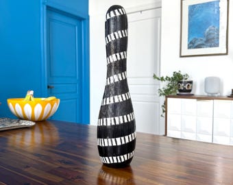 May include: A black and white striped ceramic vase with a tall, slender shape. The vase is sitting on a wooden table.