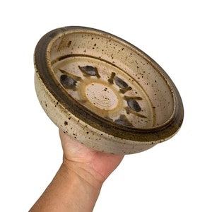 May include: A white ceramic bowl with a brown rim and speckled glaze. The bowl has a unique design with a circular pattern of holes in the centre.