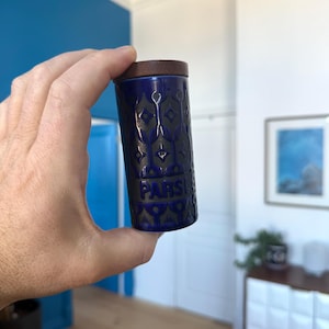 May include: A blue ceramic spice jar with a dark wood lid. The jar has a repeating geometric pattern and the word "PARSLEY" in white lettering. The jar is cylindrical and appears to be a kitchen item.
