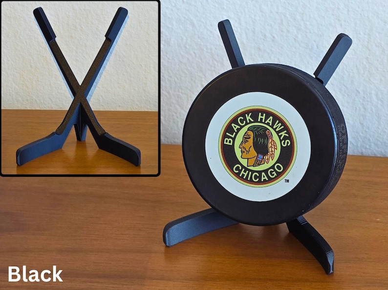 May include: Black hockey puck display stand featuring the Chicago Blackhawks logo. The stand is made of black wood and holds the puck upright. The stand has a unique design with two crossed hockey sticks.