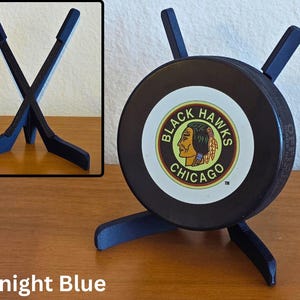 May include: A midnight blue hockey puck display stand. The stand is designed to hold a hockey puck, with a Chicago Blackhawks logo. The stand is made of a midnight blue material and has a unique design.