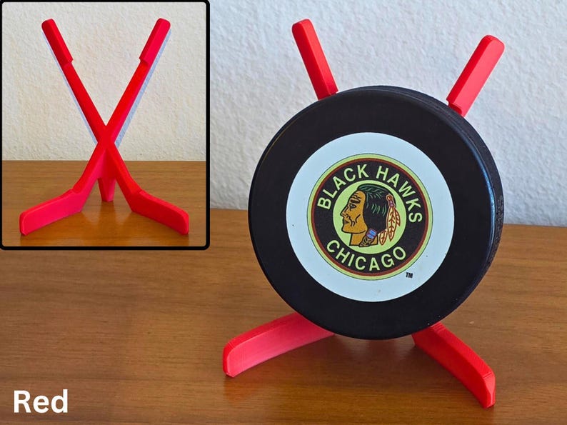 May include: A red hockey puck holder with a black puck featuring the Chicago Blackhawks logo. The holder is made of red plastic and has a unique design to display the puck. The word "Red" is at the bottom.
