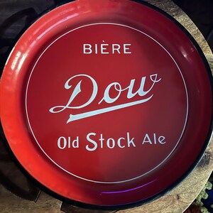 May include: Red metal tray with a black rim and a white design that says "Bière Douv Old Stock Ale".