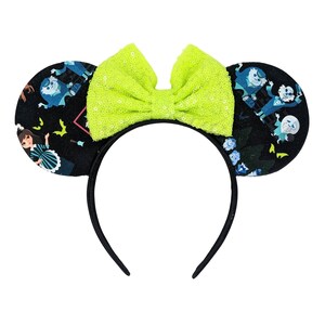 May include: Black headband with a neon green bow and two black mouse ears. The ears are covered in a black and white fabric with a pattern of a girl in a dress, bats, and a ghost.