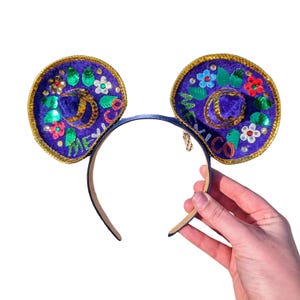Puede incluir: Orejas de Mickey Mouse de terciopelo morado con ribetes dorados y flores bordadas de colores y la palabra "México".