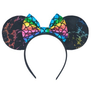 Puede incluir: Diadema con lazo de escamas de sirena arcoíris y orejas de ratón negras con purpurina.