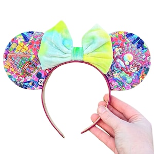 Puede incluir: Un par de orejas de ratón rosa y rojo con un estampado colorido con personajes de Disney y un lazo de teñido anudado verde y azul.