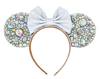May include: Silver sparkly mouse ears headband with a silver bow. The ears are covered in iridescent rhinestones.
