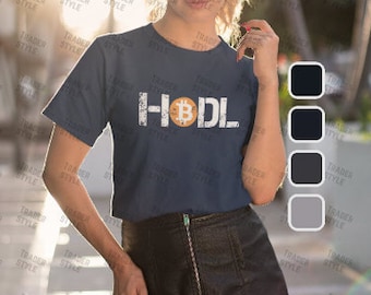 May include: A woman wearing a dark blue t-shirt with a white graphic of a bitcoin and the word "HODL". She is wearing a black skirt and has long brown hair.