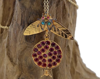 Peut inclure: Collier en or avec un pendentif en forme de grenade et un petit charme de scarabée avec des pierres précieuses turquoise et roses. Le pendentif est en or et présente un design détaillé.