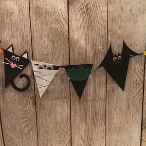 May include: A Halloween banner with six triangular flags. The flags are decorated with a pumpkin, a black cat, a mummy, a monster, a bat, and a candy corn. The flags are strung together with a white string.