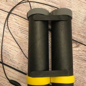 Peut inclure: Jumelles en carton noir avec une bordure jaune et un cordon noir.