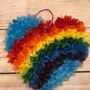 May include: A heart-shaped decoration made from tissue paper, featuring a rainbow of colours. The heart is strung with a purple ribbon.