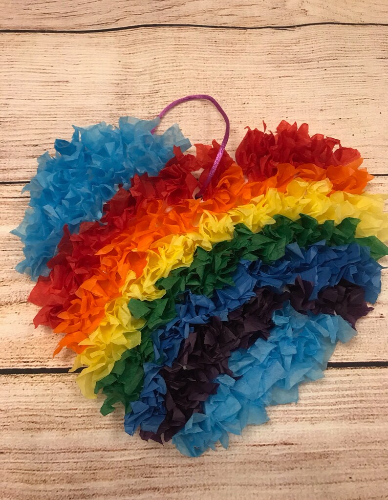 May include: A heart-shaped decoration made from tissue paper, featuring a rainbow of colours. The heart is strung with a purple ribbon.