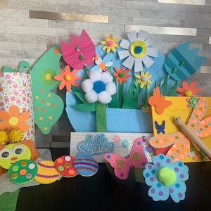 May include: A colorful spring-themed craft project with butterflies, flowers, and a dragonfly. The project includes a variety of colors, including pink, blue, green, yellow, and orange. The project also includes the words "Hello Spring" on a sign.