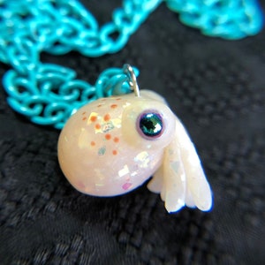 May include: A white iridescent octopus charm with a teal blue eye, hanging from a turquoise chain.