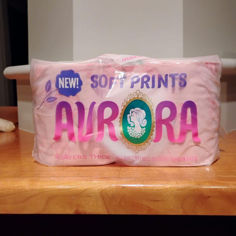 May include: A package of pink Aurora brand soft print tissues. The packaging features the word "AURORA" in large, pink letters, with "NEW!" and "SOFT PRINTS" above. A teal and gold emblem is also visible.