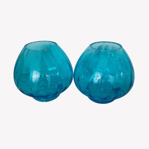May include: Two turquoise glass vases with a round shape and textured surface. The vases have a wide opening and a slightly flared base. The glass is transparent, allowing light to pass through.