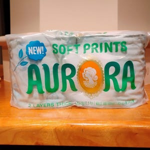 May include: A package of Aurora brand soft print tissues. The package is clear plastic, with the words "NEW! SOFT PRINTS AURORA" in green. The package contains two rolls of 2-ply tissues.