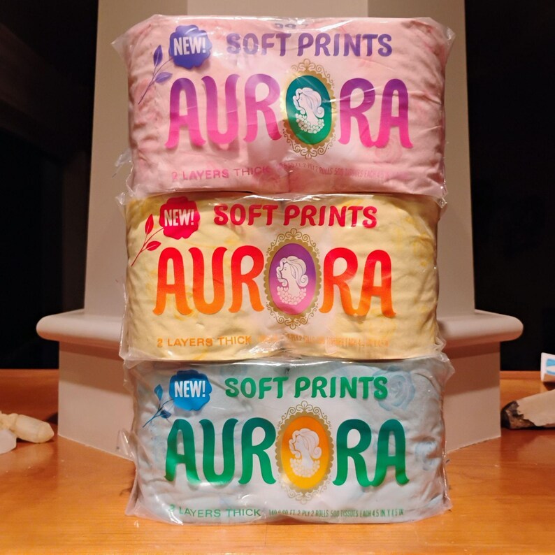 May include: Three packages of "AURORA" brand soft prints, each wrapped in clear plastic. The top package is pink, the middle is yellow, and the bottom is light blue. Each package has the words "NEW! SOFT PRINTS" and "AURORA" printed on it.