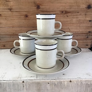 May include: Set of four white ceramic coffee mugs with brown stripes and speckles. Each mug comes with a matching saucer.