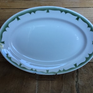 May include: A white oval serving platter with a green leaf design around the edge.