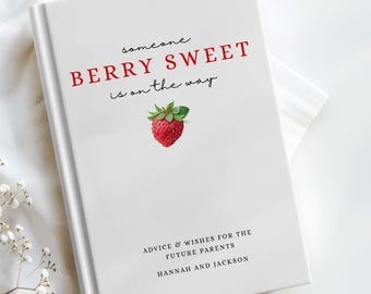 Puede incluir: Un libro blanco con el texto "BERRY SWEET is on the way" en rojo y negro, y una ilustración de fresa a la acuarela. El libro se titula "ADVICE & WISHES FOR THE FUTURE PARENTS" y está personalizado con nombres. El libro está sobre una tela blanca.