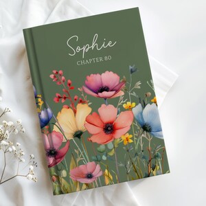 Puede incluir: Un libro de tapa dura con una cubierta verde que presenta un diseño floral. La cubierta muestra el nombre "Sophie" y "Capítulo 80" en escritura blanca. El diseño floral incluye flores rosas, rojas, amarillas y azules.