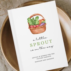 May include: A white card with the text "a little SPROUT is on the way" and a watercolor illustration of a basket of vegetables. The card is on a wooden plate. Text at the bottom reads "ADVICE & WISHES FOR THE FUTURE PARENTS HANNAH AND JACKSON."