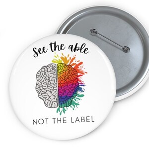 May include: White button with a rainbow brain design and the text "See the able not the label".