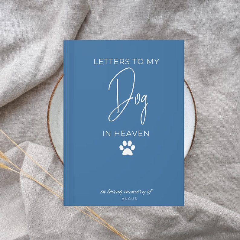 Peut inclure: Un carnet bleu avec le texte "Lettres &agrave; mon chien au paradis" et une empreinte de patte blanche. Le texte "en souvenir affectueux d'Angus" est en bas du carnet.