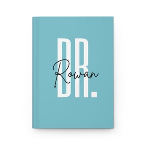 May include: A light blue journal with the text "DR. Rowan" in white and black. The journal is closed and has a clean, minimalist design. The cover is a solid light blue color.