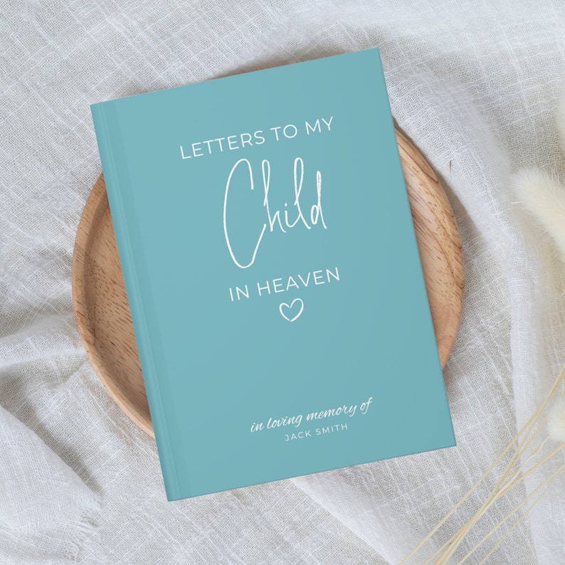 May include: A light blue journal with the text "Letters to my Child in Heaven" in white lettering. The journal has a small heart symbol and the text "in loving memory of JACK SMITH" in white lettering.