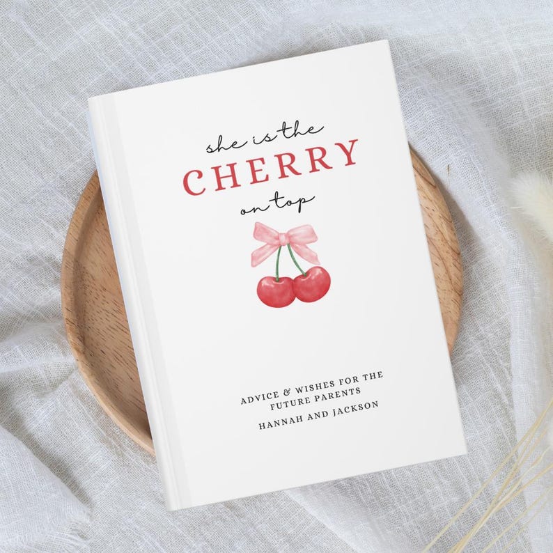 May include: A white book with the text "she is the CHERRY on top" in red and black. The book has a pink ribbon and two red cherries on the front. The text "ADVICE & WISHES FOR THE FUTURE PARENTS HANNAH AND JACKSON" is printed in black at the bottom.